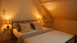 A cozy bedroom with a sloped ceiling, a bed with white linens, two bedside lamps, and a wooden nightstand. - Maison le Ber-So Close to Beauval Zoo (Selles-sur-Cher)