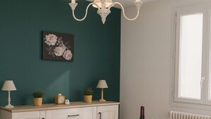 A dining area with a table set for four, a chandelier, a cabinet with decorative items, and a window with natural light. - Maison le Ber-So Close to Beauval Zoo (Selles-sur-Cher)