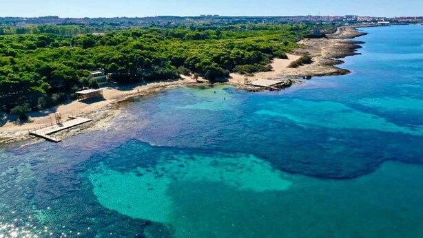 Vue aérienne d’une zone côtière avec des eaux d’un bleu limpide, une plage de sable et une végétation luxuriante.
