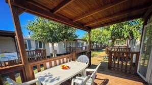 Un espace extérieur abrité, doté d’une table et de chaises, et entouré de clôtures en bois et d’arbres.