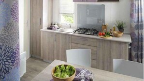 Une cuisine compacte équipée d’une cuisinière à gaz, d’un évier et de meubles en bois. On y trouve une table à manger avec des chaises et un saladier rempli de salade.