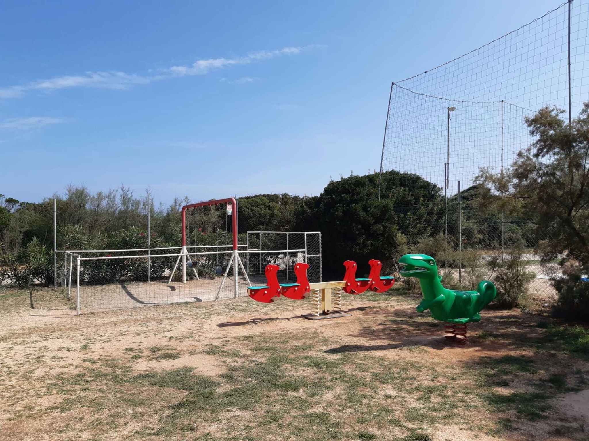 Un parque infantil con columpios, juegos para escalar y un juguete con forma de dinosaurio.