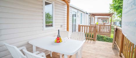 A covered outdoor patio with a white table and chairs, a bottle, and fruit.