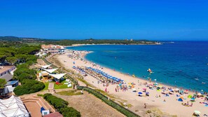 A coastal beach with a large number of beach umbrellas and people. There are buildings along the beach and a clear view of the sea. - Mobile home near the sea (Aglientu)