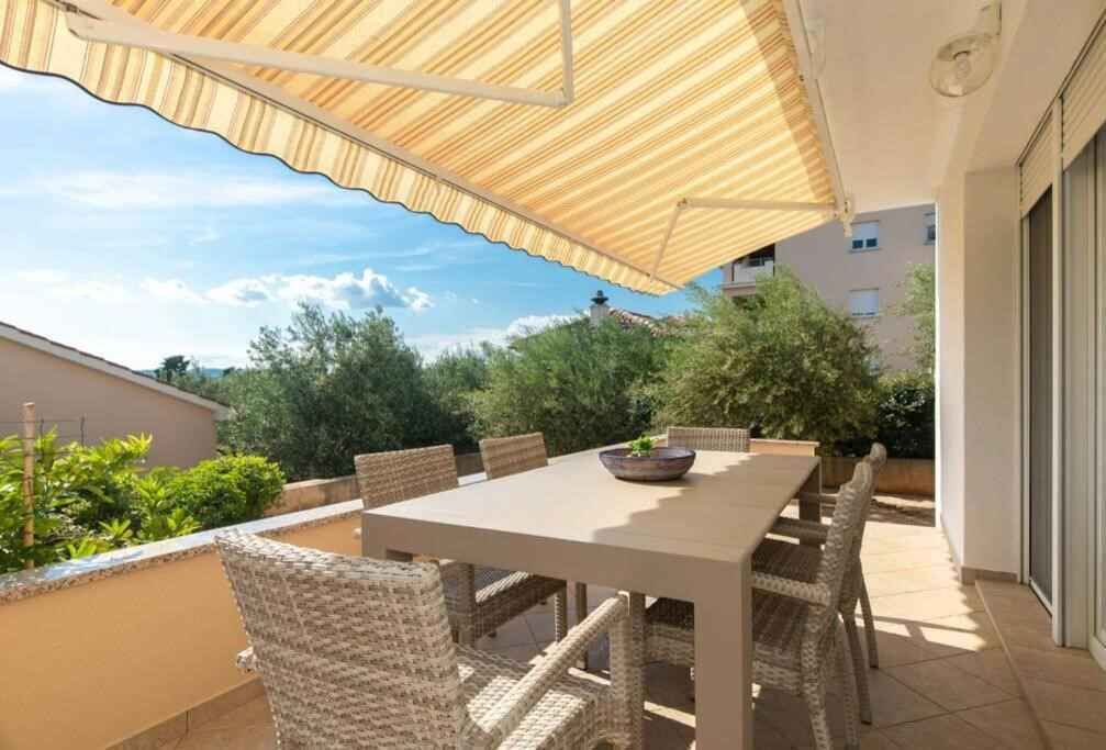 An outdoor patio with a table and chairs, a large umbrella, and a view of surrounding buildings and greenery.