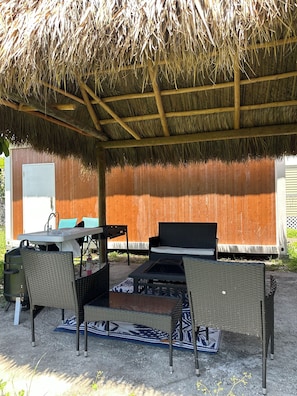 An outdoor seating area with wicker furniture, a table, and a thatched roof structure. - LUXURY MODERN STUDIO TINY HOME- PET FRIENDLY W/ AC, WiFi,FIREPLACE, FREE PARKING (North Miami)