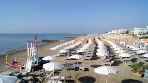 A beach with rows of white umbrellas and sun loungers, a lifeguard tower, and buildings in the background. - Holiday flat with pool (Porto Santa Margherita)