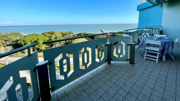 A balcony with a view of the sea, a table with chairs, and a railing with geometric cutouts. - Holiday flat with pool (Porto Santa Margherita)