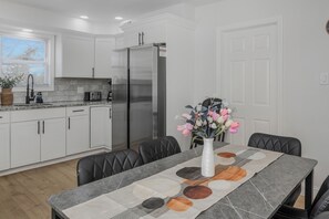 A modern kitchen with white cabinets, a stainless steel refrigerator, and a dining table with a geometric table runner. - Modern NYC Duplex with Gym,GameRoom close toTimesSq,Statueof Liberty+FreeParking (Bayonne)