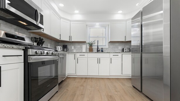 A modern kitchen with white cabinets, stainless steel appliances, and a wooden floor.