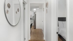 A narrow hallway with a wooden floor, a bed with white bedding, and a large mirror with heart-shaped decorations on the wall.