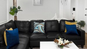 A modern living room with a black leather sofa, a white coffee table with a floral arrangement, and a large plant.