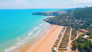 An aerial view of a coastal area with a sandy beach, a row of parked vehicles, and a hilly landscape in the background. - Mobile home with air conditioning (Peschici)