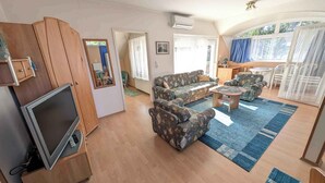 A living room with a sofa, armchairs, a coffee table, a TV, and a wooden cabinet. - Holiday apartment with large balcony, American kitchen and air conditioning (Siófok)