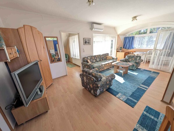 Un salon comprenant un canapé, des fauteuils, une table basse, un téléviseur et un meuble en bois.