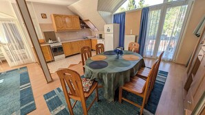 A compact kitchen with wooden cabinets, a dining table with chairs, and a view of the outdoors through large windows. - Holiday apartment with large balcony, American kitchen and air conditioning (Siófok)