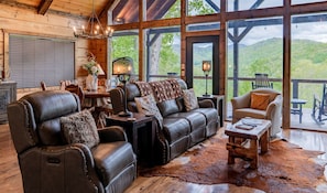 A spacious living area with leather furniture, a wooden floor, and large windows offering a view of the outdoors. - Timber Ridge-2 Bedroom, Pet Friendly, Luxury Cabin Rental, Panoramic Mountain Views, High Speed Internet, Rafting, Horseback Riding-Nantahala NC (Topton)