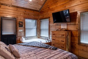 A cabin interior with a bed, a television mounted on the wall, and a window with blinds.
