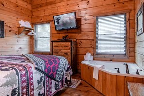 A cabin room with a bed, a television, a wooden dresser, a bathtub, and two windows with blinds. - Timber Ridge-2 Bedroom, Pet Friendly, Luxury Cabin Rental, Panoramic Mountain Views, High Speed Internet, Rafting, Horseback Riding-Nantahala NC (Topton)