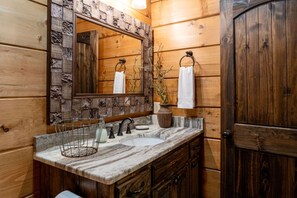 A wooden cabin-style bathroom with a large mirror, two sinks, a towel rack, and a wooden door. - Timber Ridge-2 Bedroom, Pet Friendly, Luxury Cabin Rental, Panoramic Mountain Views, High Speed Internet, Rafting, Horseback Riding-Nantahala NC (Topton)
