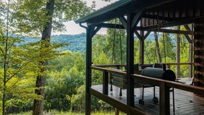 A wooden deck with a grill and seating area overlooking a forested landscape.