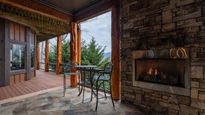 A stone fireplace, wooden deck, and outdoor seating area with a view of trees and mountains. - The Sanctuary-Pet Friendly Luxury Cabin Rental, Sits on Top of the Mountain, High Speed Internet, Hot Tub, 30 Minutes to Great Smoky Mountains, in Nantahala NC (Topton)