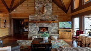 A rustic interior with a stone fireplace, wooden beams, a television, and a cozy seating area. - The Sanctuary-Pet Friendly Luxury Cabin Rental, Sits on Top of the Mountain, High Speed Internet, Hot Tub, 30 Minutes to Great Smoky Mountains, in Nantahala NC (Topton)