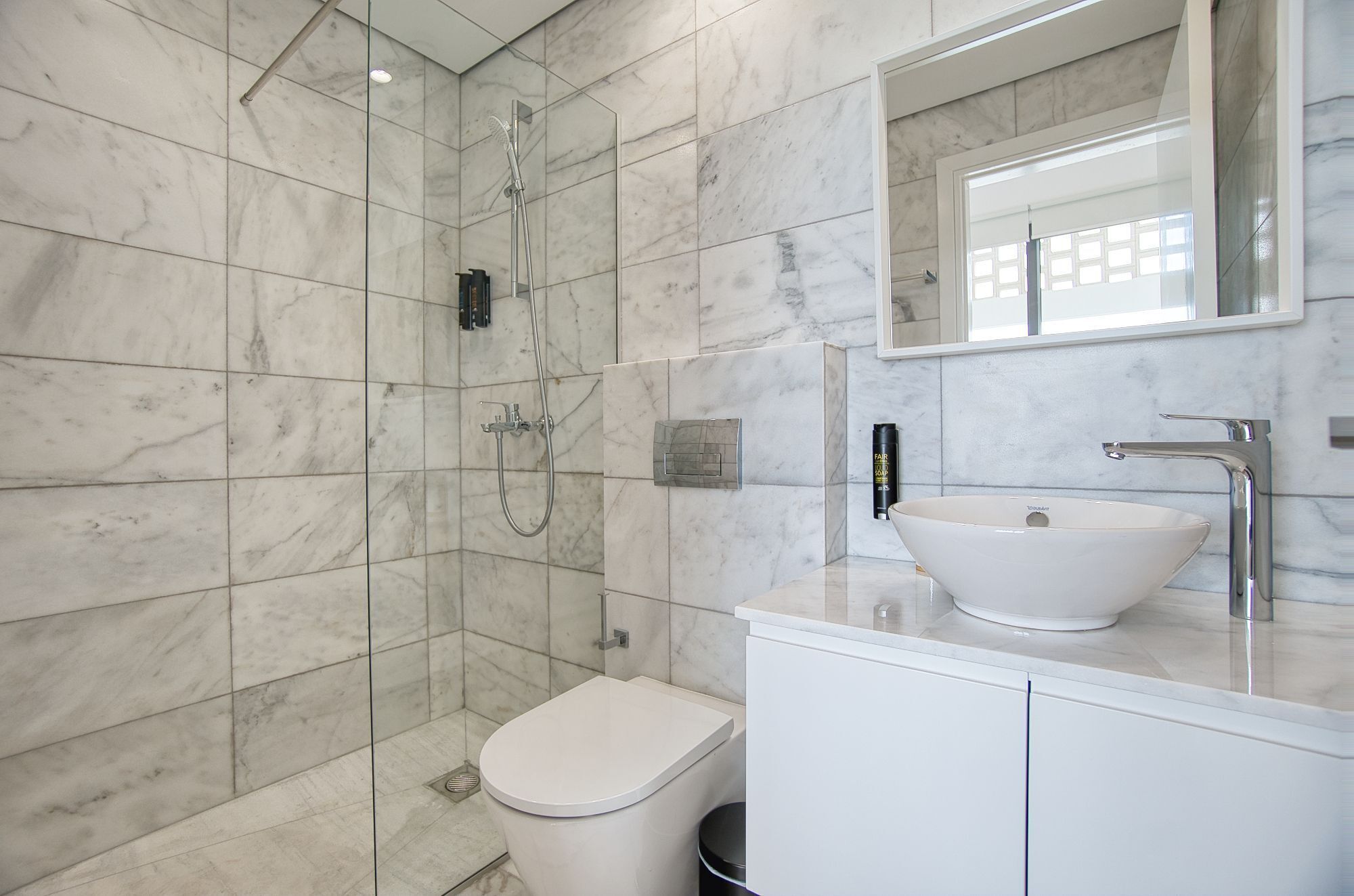 A modern bathroom with a walk-in shower, a toilet, and a sink with a large mirror above it.