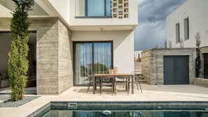 A modern outdoor pool area with a dining set and a large window overlooking the pool.