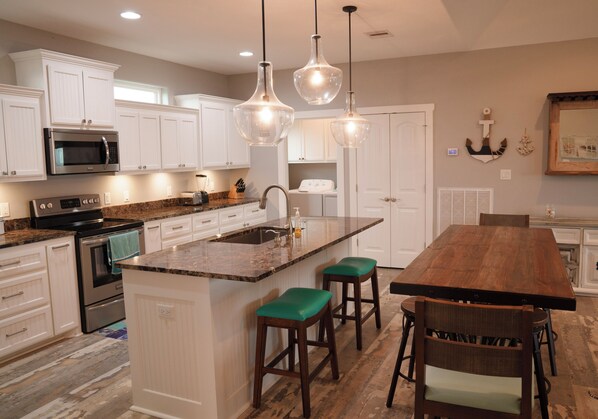 Una cocina moderna con armarios blancos, una isla central con taburetes, microondas integrado e iluminación colgante.