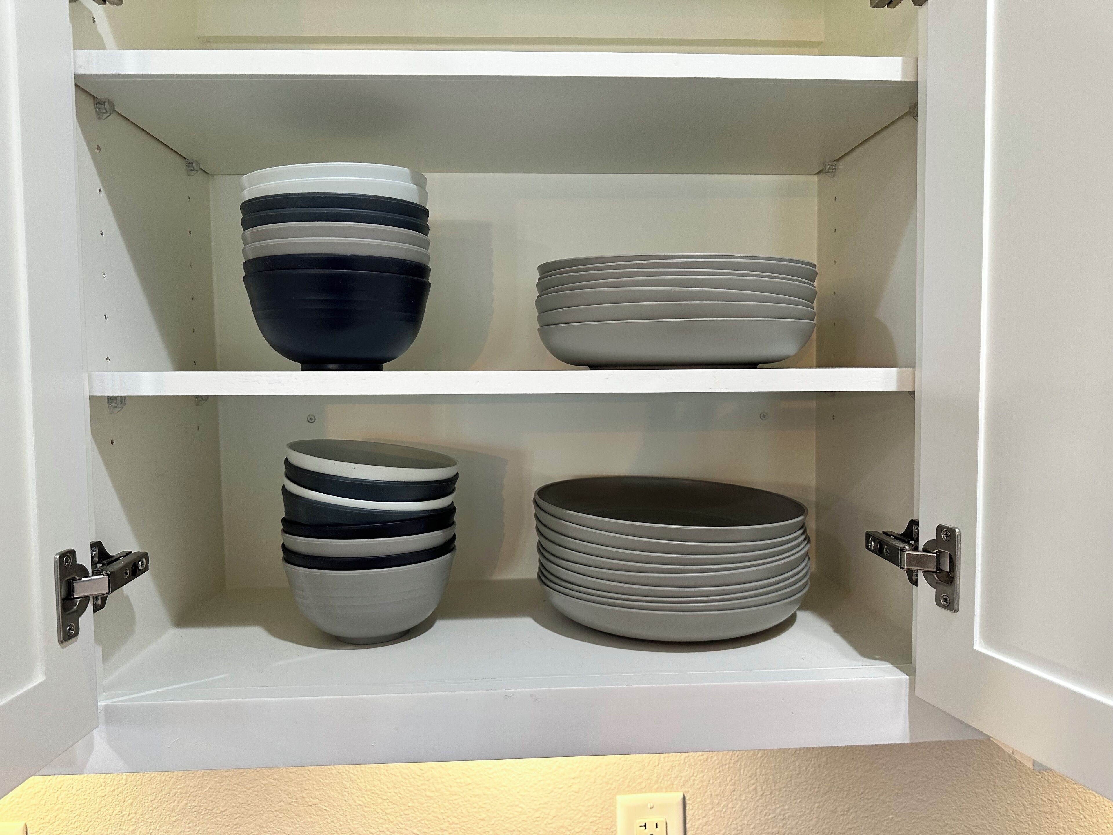 A white cabinet with two shelves, each holding stacks of bowls.