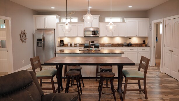 A modern kitchen with white cabinets, a central island, bar stools, and pendant lighting.