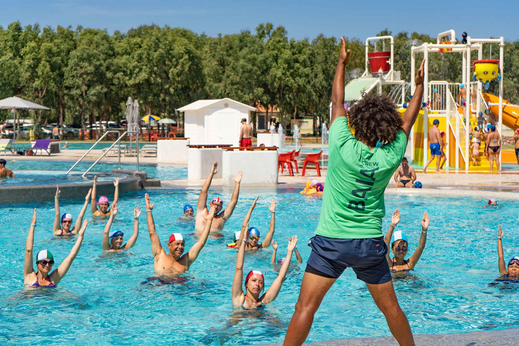 Ein Schwimmbecken mit Menschen im Wasser, einem Rettungsturm und einer Wasserrutsche.