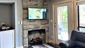 Una sala de estar con chimenea de piedra, un televisor de pantalla plana montado en la pared y un sillón de cuero negro.