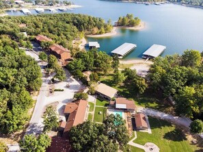 An aerial view of a lakeside property with multiple buildings, a swimming pool, and docked boats.