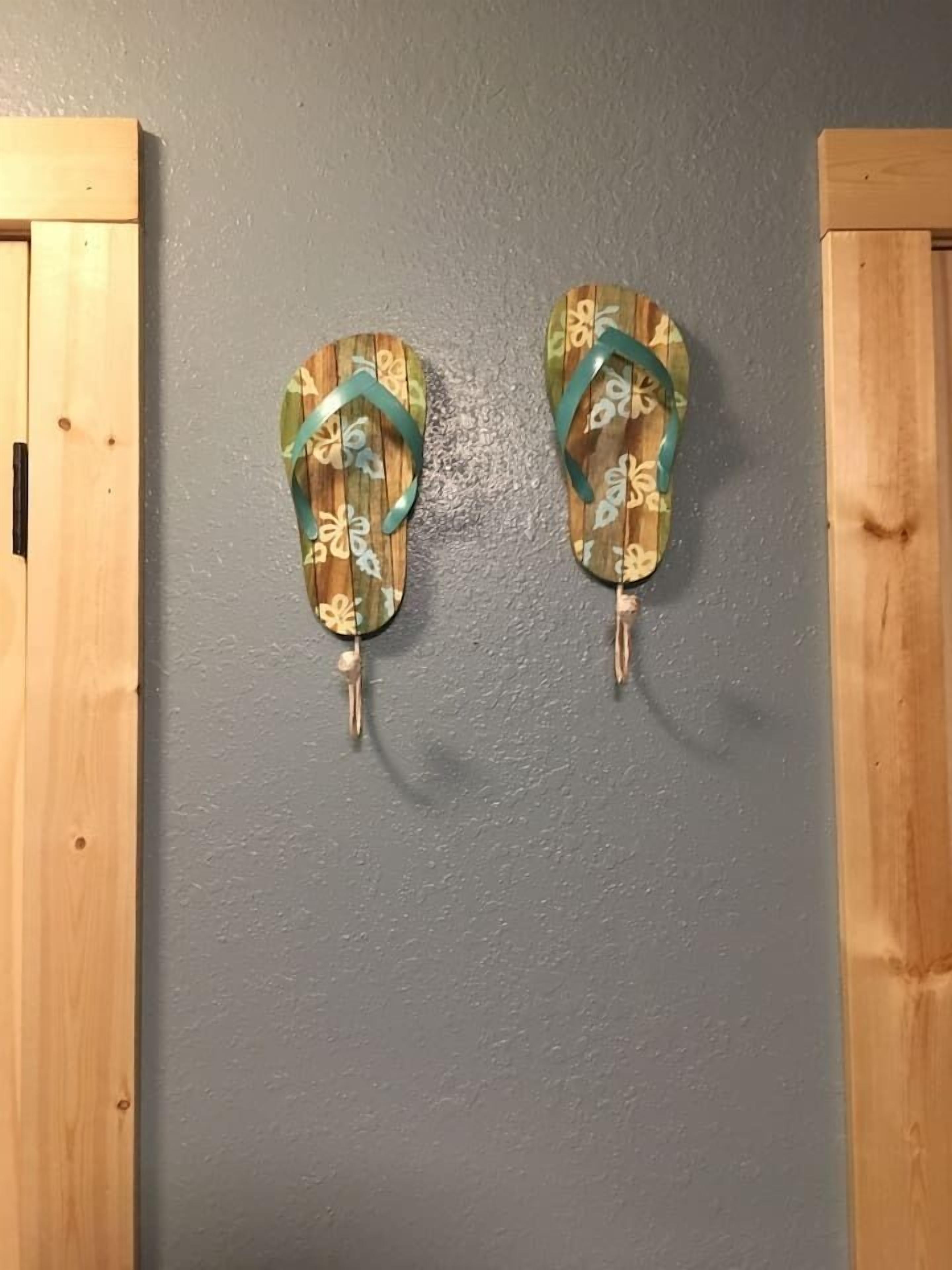 A pair of wooden flip-flops with a floral pattern hanging on a gray wall.