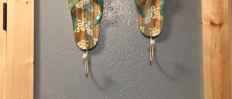 A pair of wooden flip-flops with a floral pattern hanging on a gray wall.