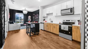 Una cocina moderna con armarios blancos, microondas, horno y un comedor con un taburete negro.