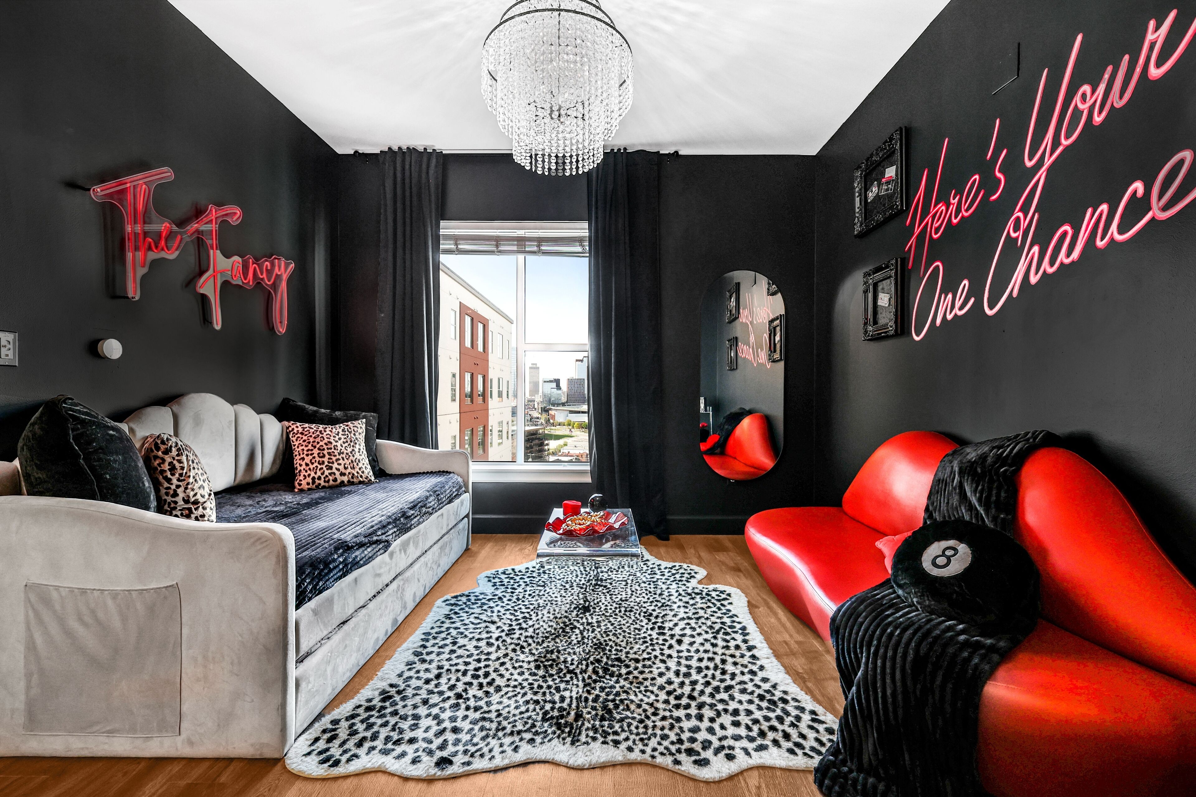 Una sala de estar moderna con un sofá, un sofá rojo, una araña y vistas de la ciudad.