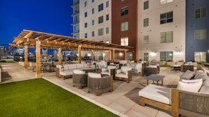 Un patio al aire libre con varios conjuntos de asientos, incluyendo sofás y sillones, bajo una pérgola de madera.