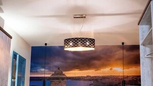 Un dormitorio con una cama grande, una lámpara colgante y un mural con un atardecer sobre un paisaje urbano.