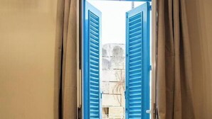 Una habitación con una puerta azul, una pequeña mesa redonda, un sofá azul y vistas a un edificio de piedra a través de la puerta abierta.