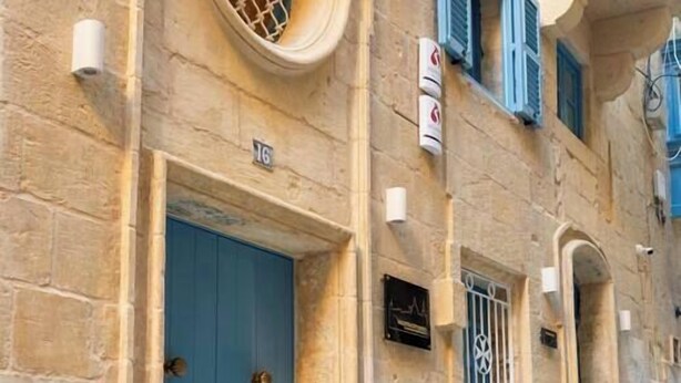 Un edificio de piedra con una puerta azul, el número 16, y un pequeño ventanal con una reja de metal.