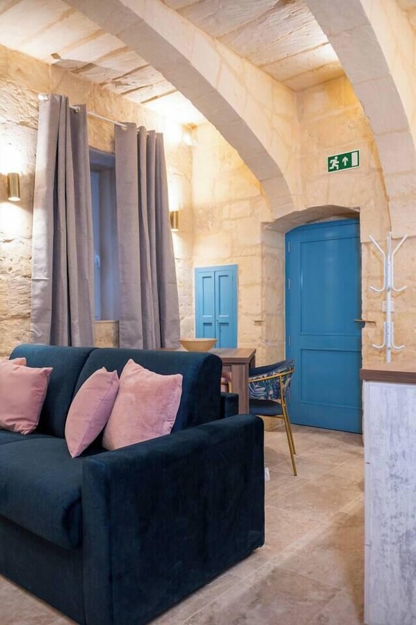 A cozy room with a dark blue sofa, stone walls, a blue door, and a green exit sign.