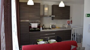 A compact kitchen with dark wood cabinets, a gas stove, a sink, and two pendant lights. - Pilgrim's Rest Penthouse (Gzira) (Gzira)