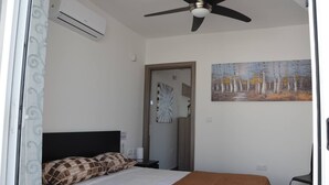 A bedroom with a bed, a ceiling fan, an air conditioning unit, a painting, and a door leading to another room. - Pilgrim's Rest Penthouse (Gzira) (Gzira)