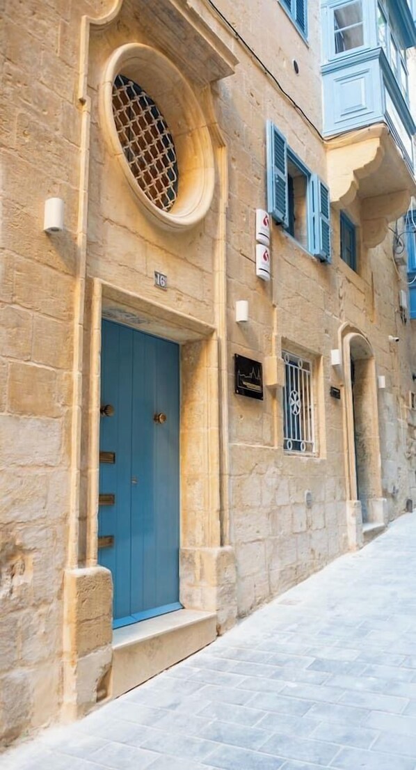 A stone building with a blue door, numbered 16, and a small window with metal bars.