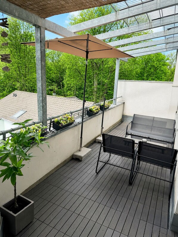 An outdoor balcony with a table and chairs, a hanging umbrella, and potted plants.