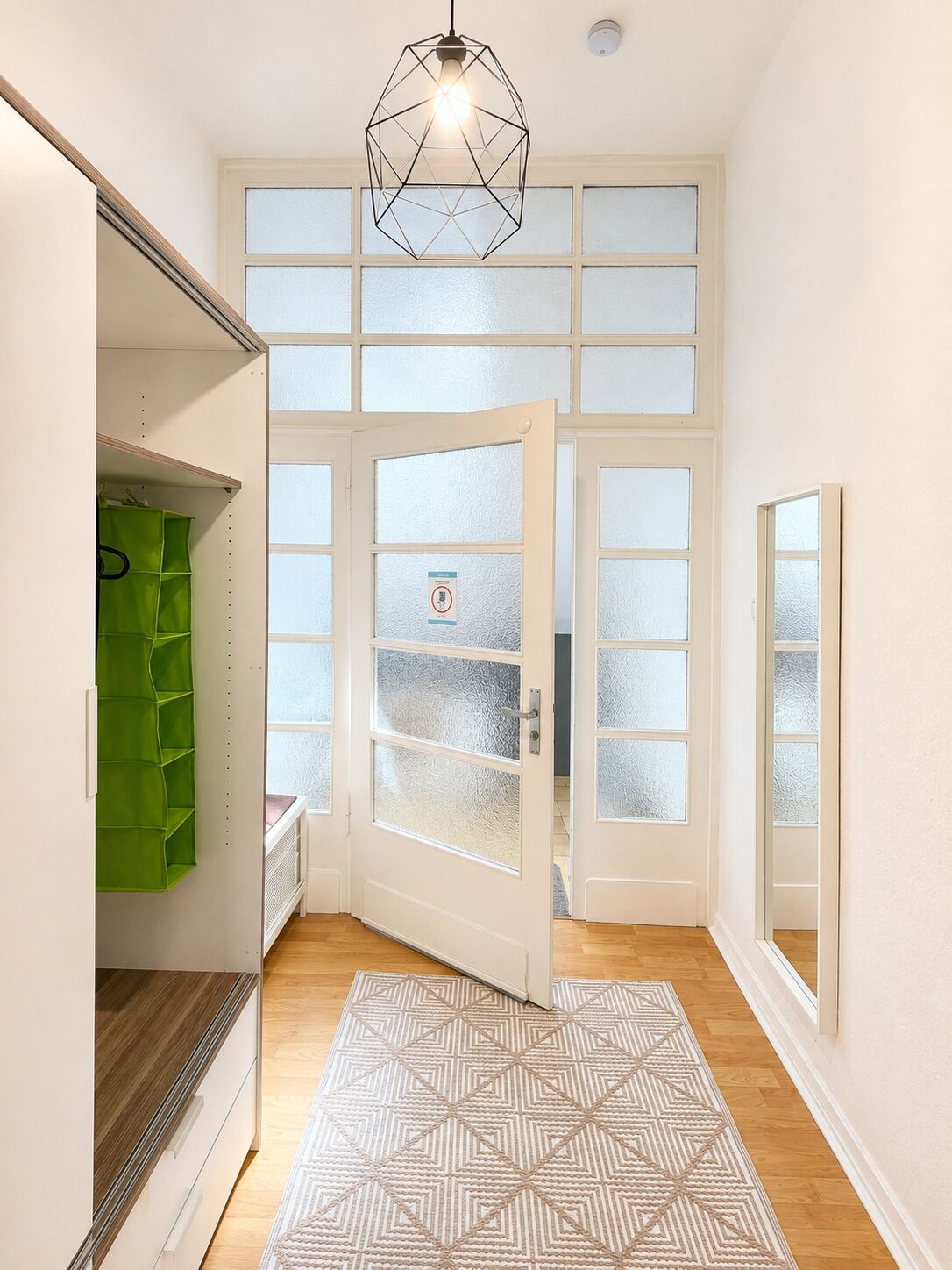 Ein Flur mit einem geometrisch gemusterten Teppich, einer grünen Stauraum-Einheit und einer Tür mit satinierten Glasscheiben.