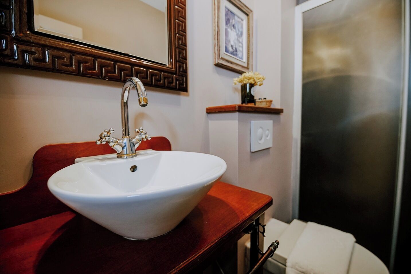 Een badkamer met een wit wastafelmeubel, een rode vanity, een spiegel met decoratieve lijst, een klein plankje met een vaas en een douchegedeelte.